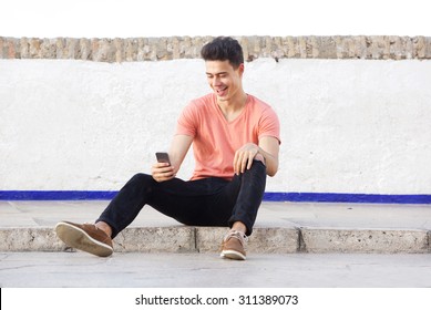 Portrait Of A Cool Guy Sitting On Sidewalk Looking At Mobile Phone