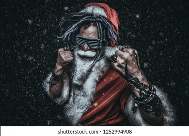 Portrait of a cool punk Santa Claus in luminous glasses with bright dreadlocks over black background.