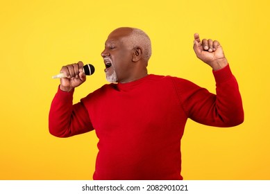 Portrait Of Cool Senior Black Man Singing Song, Using Microphone, Performing Karaoke On Orange Studio Background. Elderly African American Male Singer Giving Live Music Concert