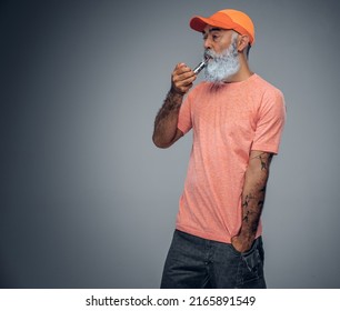 Portrait Of Cool Senior Man Dressed In Casual Attire And Baseball Cap Smoking Vape.