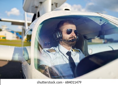 Portrait von coolen jungen Piloten sitzen in Privatflugzeugen bereit zum Start. Heller Sommertag, gut aussehendes männliches Modell