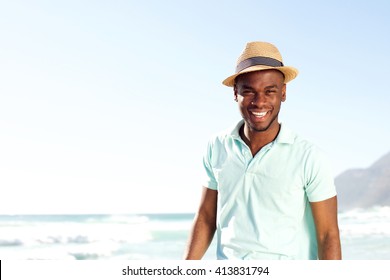 Portrait of cool young african man with hat smiling at the beach in summer