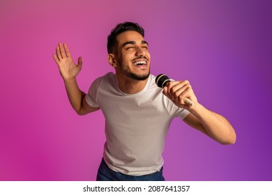 Portrait Of Cool Young Arab Man Singing Song, Using Microphone, Performing Karaoke In Neon Light. Millennial Middle Eastern Male Singer With Mic Giving Live Music Concert