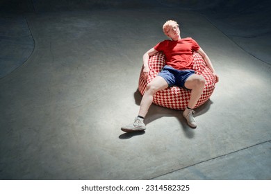 Portrait cool young man sitting, relaxing on bean bag chair on concrete sports ramp - Powered by Shutterstock