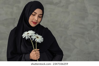 Portrait with copy space adult beautiful muslim woman wearing black headscarf, traditional dress, smiling with happiness, holding pure white flowers, showing innocence, beauty. Diversity Concept - Powered by Shutterstock