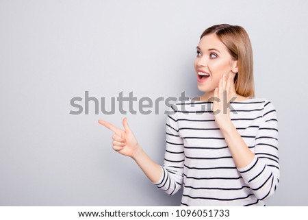 Portrait with copy space for advertisement of attractive, amazed, stylish, impressed, funny girl with open mouth holding palm near face pointing forefinger to empty place isolated on grey background