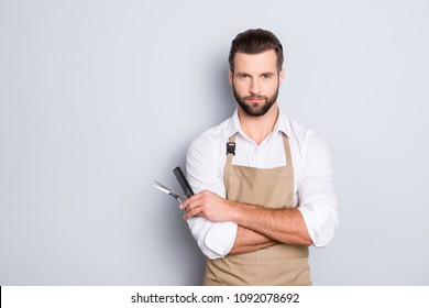 Portrait with copy space, empty place of virile harsh barber having his arms crossed, holding equipments in hand, looking at camera, isolated on grey background