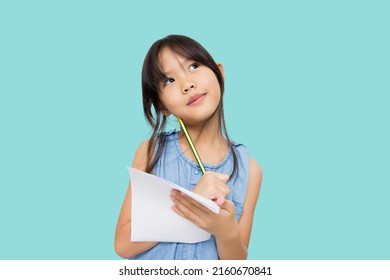 Portrait With Copy Space Empty Place Of Thoughtful Little Asian Girl Having Paper And Pencil In Hands Looking Up, Writer Waiting For Muse, Isolated On Green Background