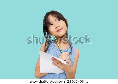 Portrait with copy space empty place of thoughtful little Asian girl having paper and pencil in hands looking up, writer waiting for muse, isolated on green background