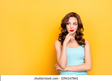 Portrait with copy space of thoughtful doubtful girl with modern hairdo looking at empty place holding hands on chin isolated on yellow background