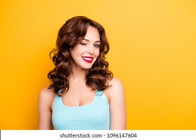Portrait with copyspace empty place of foxy funny girl with modern hairdo winking with one eye having beaming smile red pomade lipstick isolated on yellow background