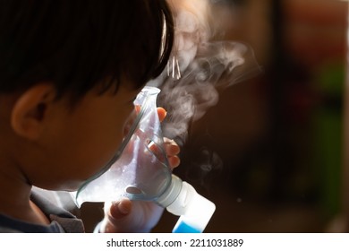 Portrait Of A Coughing Child Who Is Doing Aerosol. Close-up Of The Nebulizer With The Steam Coming Out Against The Light