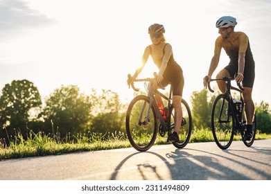 Portrait of a couple of athletes dressed in activewear biking on paved road. Countryside area, sunny day outdoors. Professional road bicycle racers in action while riding outside of the city. - Shutterstock ID 2311494809