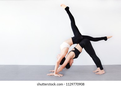 Portrait Of Couple Beautiful Young Women Wearing Sportswear Practicing Yoga In Studio,natural Light.Concept : Partner Yoga Poses For Beginner.Downward Facing Dog And Handstand Pose.