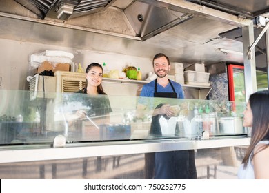 Portrait of a couple of food truck owners working and cooking some food for a customer - Powered by Shutterstock
