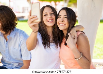 Portrait of a couple of Hispanic girlfriends taking a selfie with a smartphone at school