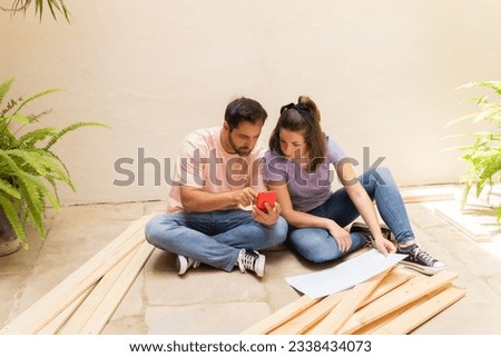 Portrait Of Couple, looking at smartphone instructions of disassembled pieces of furniture in new house.