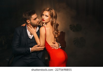 Portrait couple in love man and woman embracing hugging fashion model posing. luxurious male black suit costume. girl in elegant evening red dress open naked sexy back. Modern stylish guy dark room