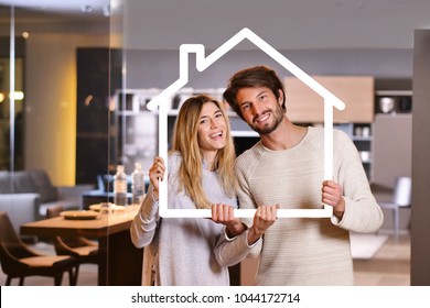 Portrait Of A Couple In Love Who Have Just Bought A House And Is Moving. The Bride And Groom Smile And Hold And Hold The Outline Of A House The In Their Hands. Concept Of: Home, Family, Ecology