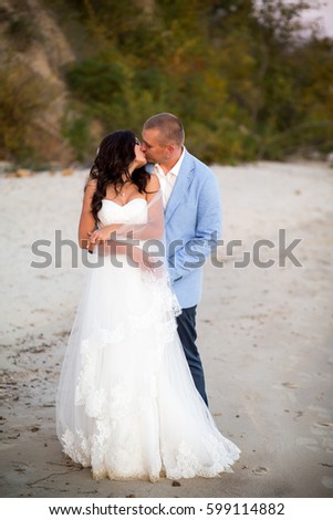 Portrait of Couple of lovers newlyweds on the seafront. Brunette bride in wedding dress with a beautiful hairstyle, veil and makeup and her husband