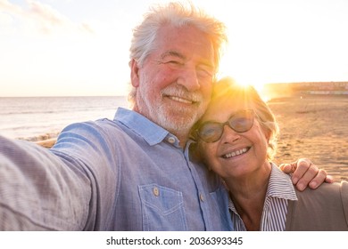 Portrait of couple of mature and old people enjoying summer at the beach looking to the camera taking a selfie together with the sunset at the background. Two active seniors traveling outdoors. - Powered by Shutterstock