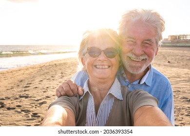 Portrait of couple of mature and old people enjoying summer at the beach looking to the camera taking a selfie together with the sunset at the background. Two active seniors traveling outdoors. - Powered by Shutterstock