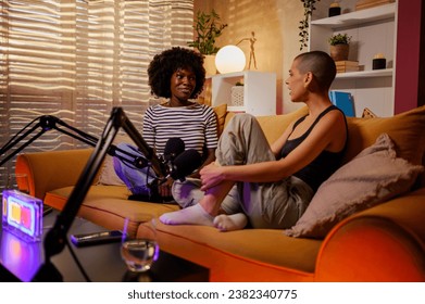 Portrait of a couple multiracial women co-hosts discussing important topics live on air while recording a podcast episode in a cozy studio on a yellow sofa. Focus on an african american woman. - Powered by Shutterstock