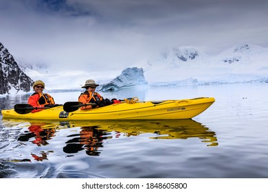 Portrait Of A Couple Of Smiling Older Antarctic Cruise Passengers Having Fun In A Kayak, With Beautiful Mountains And Glaciers Reflected In Neko Harbour, Antarctic Peninsula, Antarctica 12.07.17