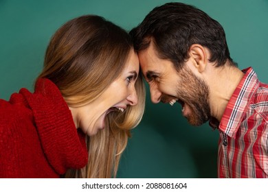 Portrait Of Couple Standing, Bumping Heads Together, Screaming And Looking At Each Other Isolated Over Green Background. Concept Of Love, Relationship, Facial Expression, Emotions, Feelings And Ad