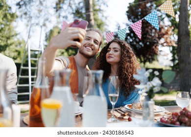 Portrait of couple taking selfie, sitting at the table with family and friends at the family garden party. - Powered by Shutterstock