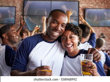 Portrait Of Couple Watching Game In Sports Bar On Screens