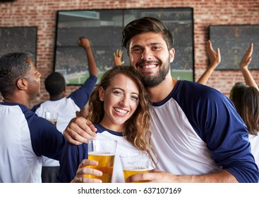 Portrait Of Couple Watching Game In Sports Bar On Screens