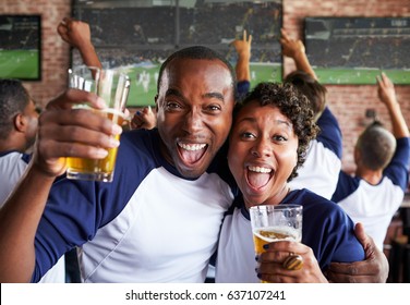 Portrait Of Couple Watching Game In Sports Bar On Screens