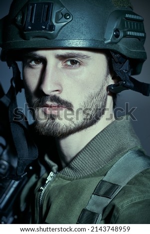 Portrait of a courageous soldier in Combat Uniform and helmet looking calmly and resolutely at the camera. Studio portrait on a grey background. 