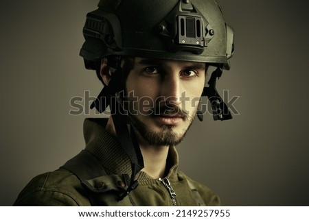 Portrait of a courageous soldier in Combat Uniform and helmet looking resolutely at the camera. Studio portrait on a grey background. 