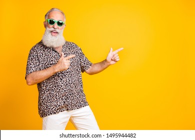 Portrait of crazy funny funky old bearded man with eyeglasses eyewear point at copyspace recommend sales discounts  wear leopard print shirt isolated over yellow  background