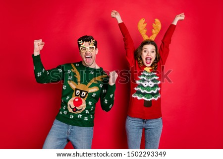 Portrait of crazy funny two family wife husband brown hair celebrate victory raise fists scream yes wear christmas tree design pullover jeans costume spectacles isolated over red color background