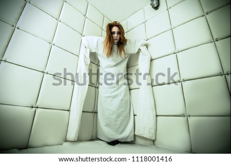 Portrait of a crazy girl dressed in a straitjacket in an isolated room in a madhouse.