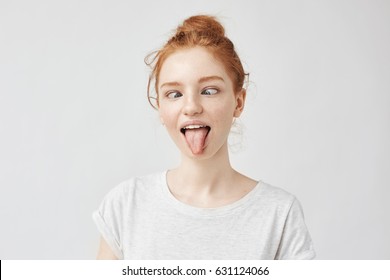 Portrait of crazy and silly yet beautiful freckled girl with eyes crossed, puting out toungue fooling around. Pretending being at audiologist. Easy lifestyle concept on white.