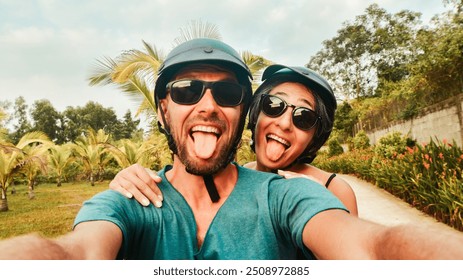 Portrait crazy smiley young happy caucasian couple take smartphone selfie while having fun driving scooter on tropical road trip in southeast asia. Couple in love having fun travel in asia - Powered by Shutterstock