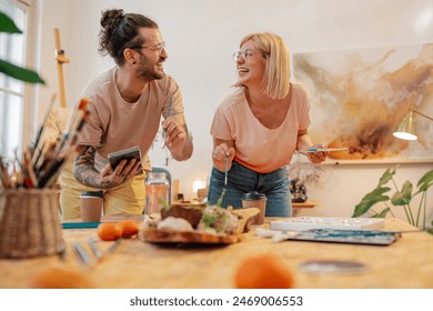 Portrait of a creative hipster couple standing at atelier and creating an artwork together while smiling at each other. A young happy trendy artistic couple painting together at art studio. Copy space - Powered by Shutterstock