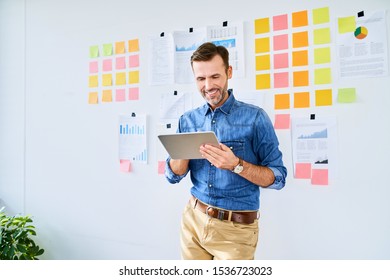 Portrait of creative office worker  using tablet and leaning against office wall
