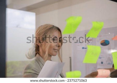 Portrait of creative professionals looking over a postit note wall and brainstorming. Business women standing at the office behind glass wall with sticky notes.