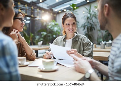 Portrait Of Creative Team Collaborating On Project During Meeting In Outdoor Cafe, Focus On Smiling Businesswoman Wearing Glasses, Copy Space