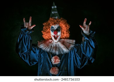 Portrait of a creepy scary clown in a bloody circus costume and a red wig. Black background. Horror. Halloween.