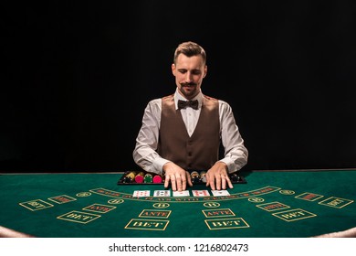 Portrait of a croupier is holding playing cards, gambling chips on table. Black background