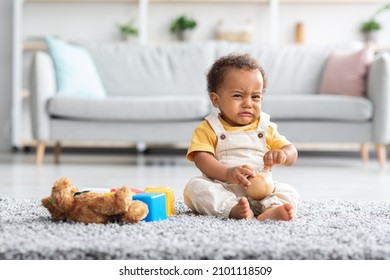 Portrait Of Crying Cute African American Infant Boy Sitting On Floor In Living Room, Upset Black Toddler Child Wearing Jumpsuit Whining And Sobbing At Home, Feeling Sad And Lonely, Copy Space