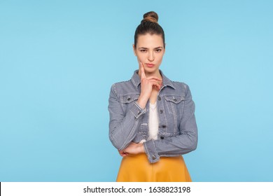 Portrait of cunning smart fashionably dressed woman with hair bun looking at camera and thinking over revenge, scheming evil plan, sly prank, cheats. indoor studio shot isolated on blue background