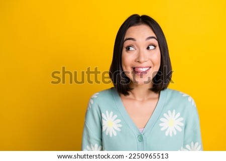 Portrait of cunning tricky girl with straight hairstyle wear blue cardigan look empty space lick teeth isolated on yellow color background