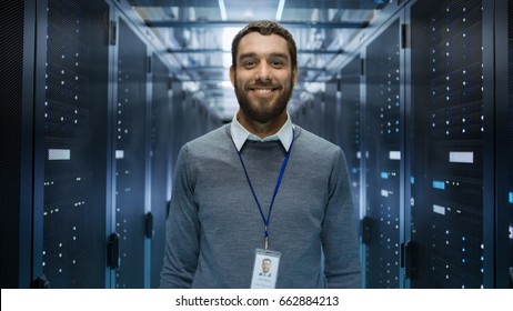 Portrait Of A Curios, Positive And Smiling IT Engineer Standing In The Middle Of A Large Data Center Server Room.